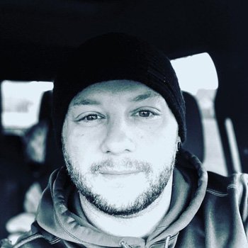 Matt Volkmann shown in a black & white image wearing a toboggan and smiling.